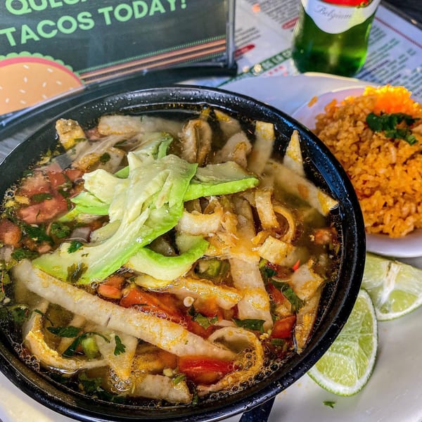 A bowl of Mexican tortilla soup with avocado, tomatoes, and cilantro, served with rice and lime.