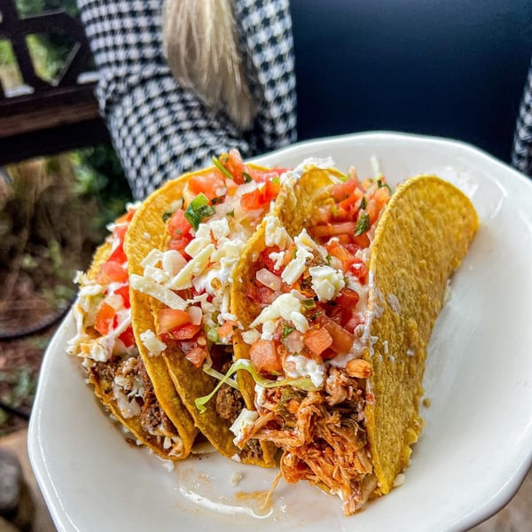 Three Cantina Caramba! tacos with various fillings, pico de gallo, and cheese on a white plate.