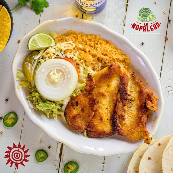Grilled chicken with rice, guacamole, onions, jalapeños, and lime on a white plate.