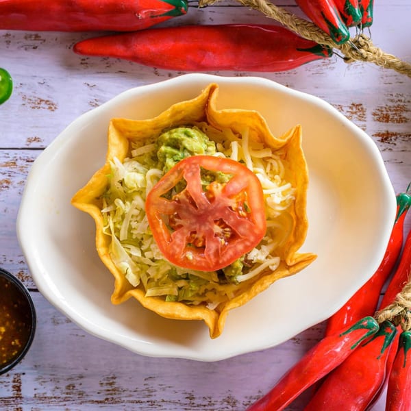 Taco salad in a crispy tortilla bowl with lettuce, guacamole, cheese, and a tomato slice.