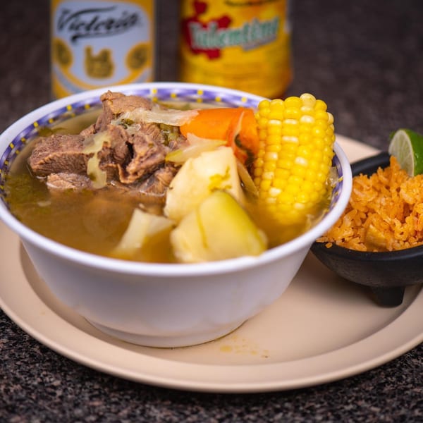 Hearty Mexican beef soup with corn, potatoes, carrots, and a side of red rice and lime.